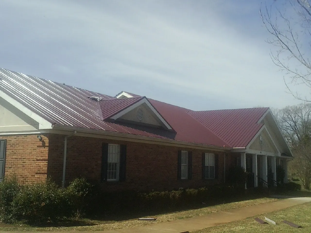 Red metal roof with gabled entries on a long brick building, from a Hail Damage Roof Repair job in Sharpsville