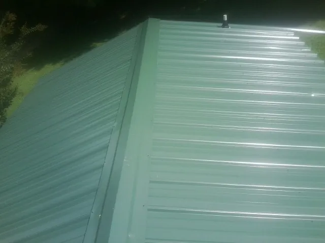 New green metal panels meeting at the ridge of a roof — Flat Roof Repair work by our crew in Sharpsville