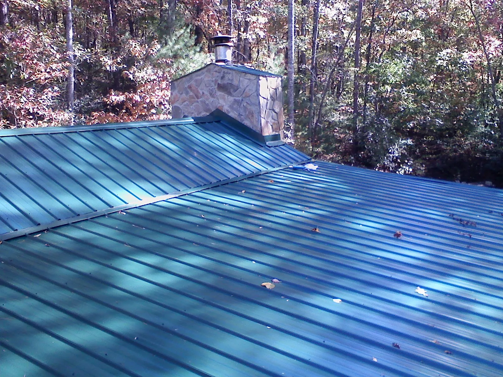 New green metal roof and stone chimney surrounded by autumn woods in Sharpsville