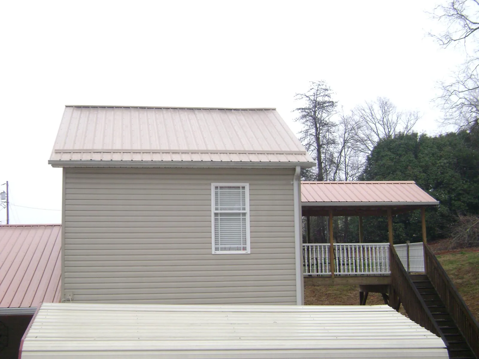 Tan metal roofs on a two story addition and attached porch, from a Roof Replacement job in Sharpsville